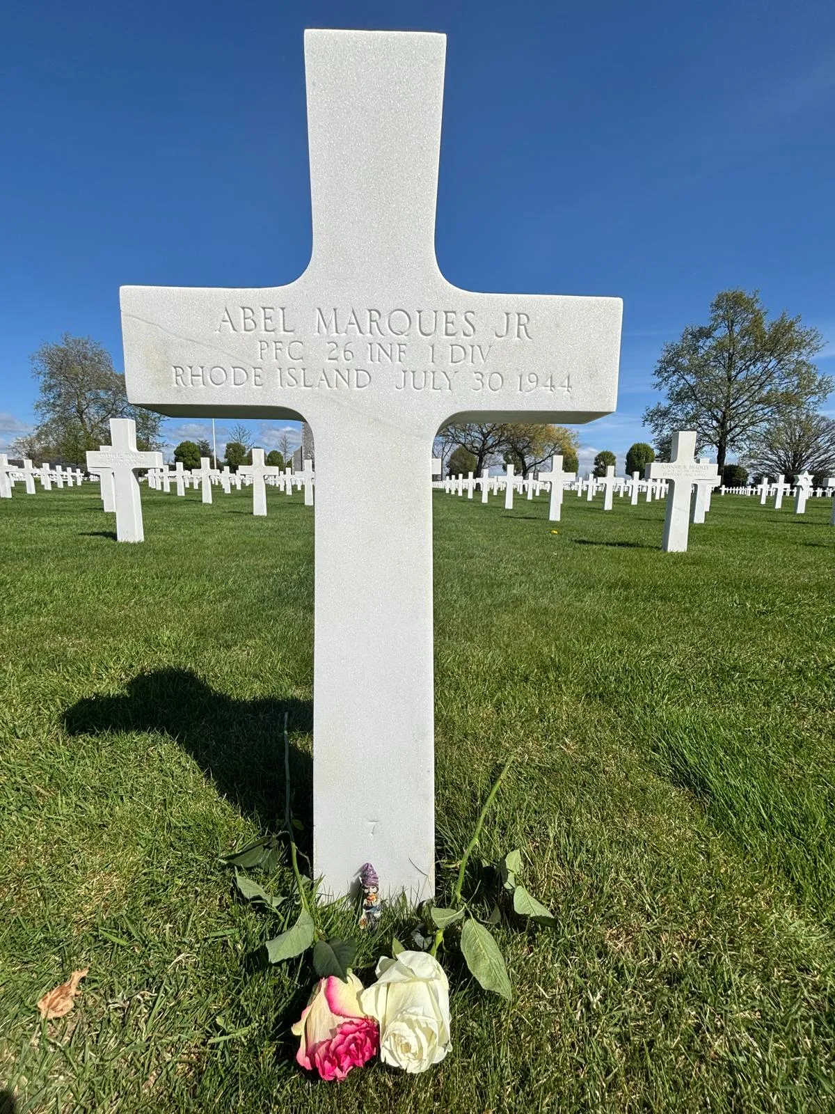 Pink and white roses laid at the base of Abel's cross, with a small figurine nearby