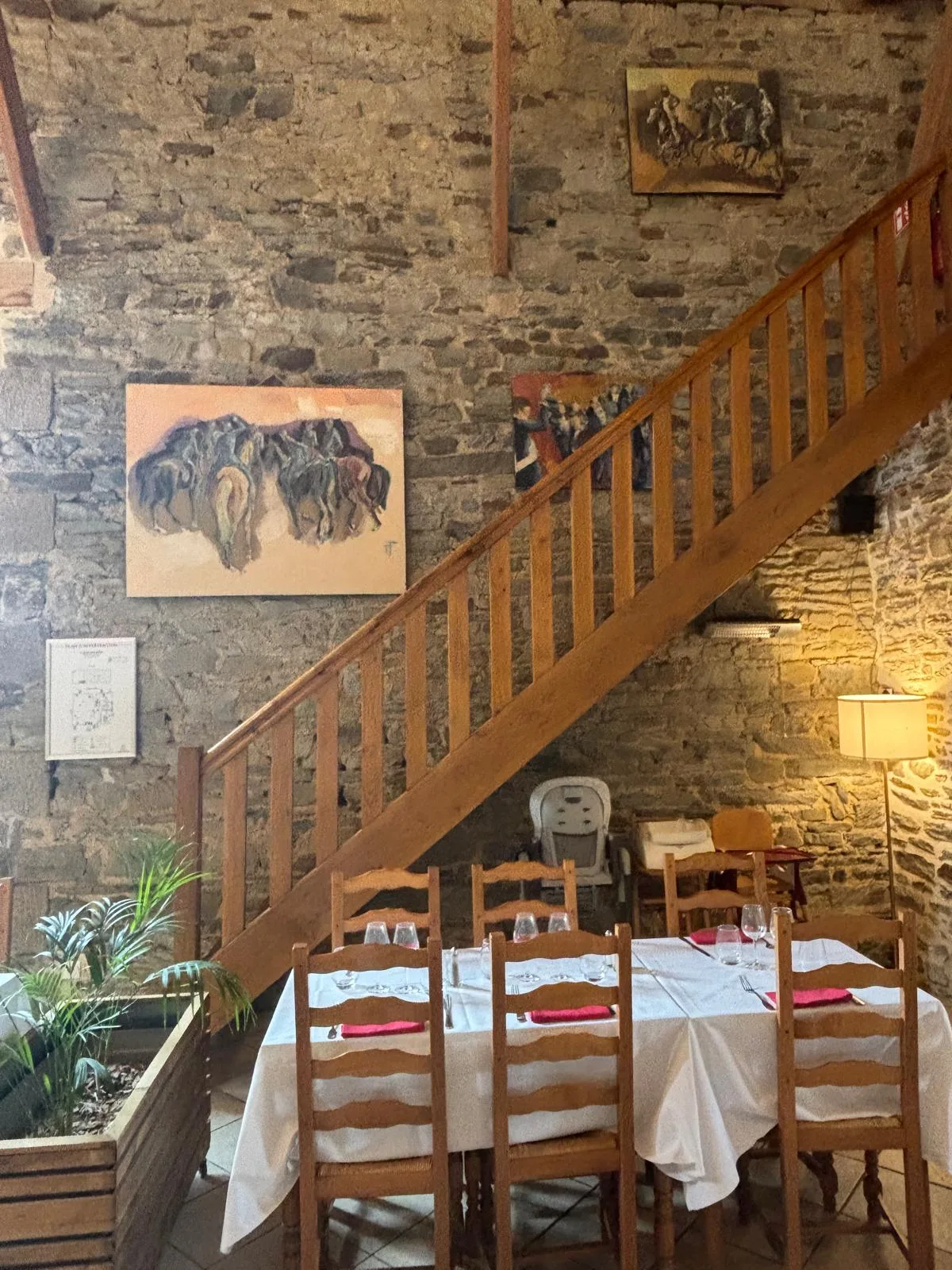 A table set beneath the wooden staircase and stone wall hung with paintings