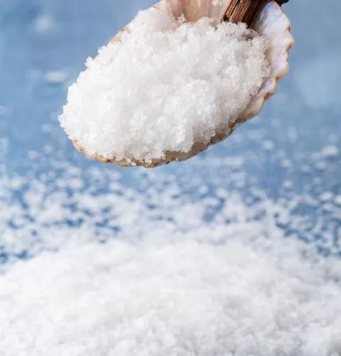 Fleur de sel de Guérande crystals lifted in a shell scoop above a bed of coarse salt